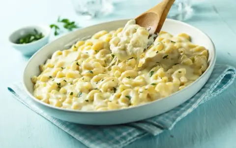 Kremowe makaronowe danie, idealne do przygotowania z przepisu na mac and cheese. Łyżka wydobywa porcję ciągnącego się sera.