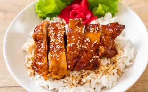 Pyszny kurczak w miodzie, polany sosem teriyaki i posypany sezamem, podany na ryżu z dodatkiem sałaty i marynowanego imbiru.