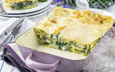 Pyszne lasagne ze szpinakiem i beszamelem, zapieczone na złoto, w fioletowym naczyniu. Idealna na rodzinny obiad.