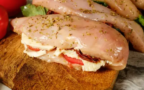 Nadziewana pierś z kurczaka z mozzarellą i suszonymi pomidorami, przyprawiona ziołami, gotowa do pieczenia.