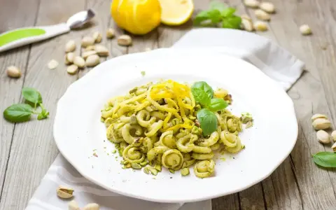 Makaron z zielonym pesto, którego głównym składnikiem są pistacje, ozdobiony skórką cytrynową i listkami bazylii.