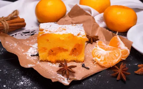 Puszyste ciasto z mandarynkami, posypane cukrem pudrem, obok świeże cząstki owoców i gwiazdki anyżu.