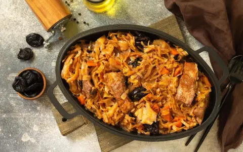 Pyszny bigos z kiszonej kapusty z kawałkami mięsa i śliwkami, podany w żeliwnym naczyniu.