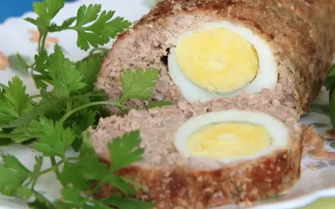 Pyszna pieczeń rzymska w sosie, z jajkiem w środku, udekorowana natką pietruszki.