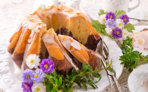 Modne ciasta na Wielkanoc: marmurkowa babka z lukrem i migdałami, ozdobiona wiosennymi kwiatami i zielenią.