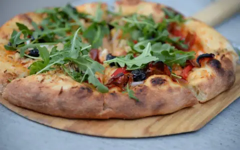 Pyszna pizza z rukolą i oliwkami na drewnianej desce. Proste ciasto na pizzę zawsze wychodzi, tworząc idealną bazę dla ulubionych dodatków.