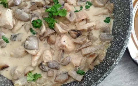 Pyszny kurczak z pieczarkami w sosie śmietanowym, udekorowany natką pietruszki, gotowy do podania.
