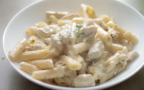 Penne w kremowym sosie serowym z kawałkami kurczaka, udekorowane gałązką ziół. Pyszny makaron serowy z kurczakiem.