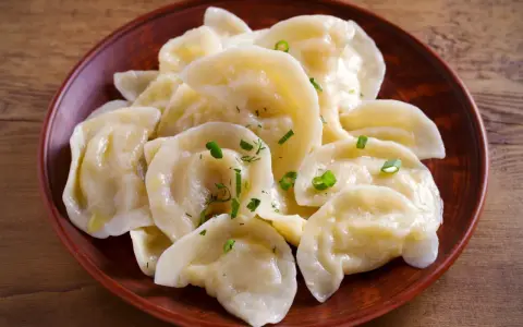 Pyszne pierogi z tradycyjnym farszem do uszek, posypane szczypiorkiem, na glinianym talerzu.