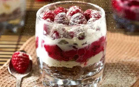 Pyszne desery w pucharkach z malinami i kremem, posypane cukrem pudrem. Na łyżeczce malina.