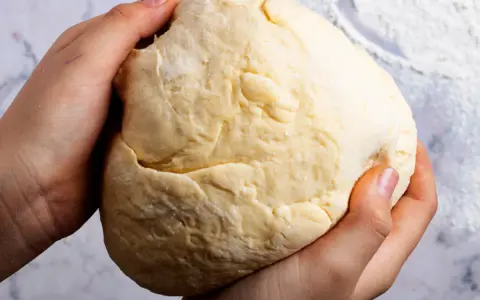 Dłonie formują puszyste ciasto drożdżowe na suchych drożdżach, gotowe do pieczenia.