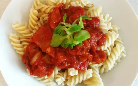 Fusilli z sosem pomidorowym i pomidorkami koktajlowymi, udekorowane świeżą zieleniną. Pyszne danie gotowe w kilka minut.