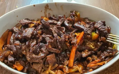 Pyszne wołowina stir fry z warzywami i makaronem, podane w białej misce.