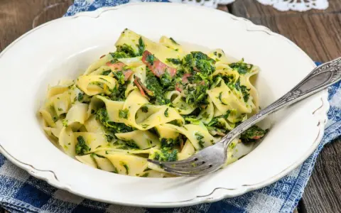 Pappardelle z boczkiem i szpinakiem, danie pełne smaku, podane na talerzu z widelcem.