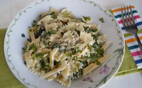 Pyszny makaron z pesto i tuńczykiem, posypany świeżą natką pietruszki, podany na talerzu z ozdobnym brzegiem.