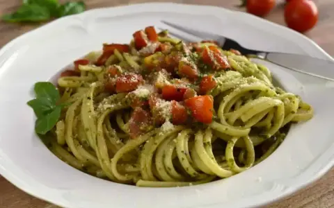 Pyszny makaron z pesto, pomidorkami i parmezanem, udekorowany listkiem bazylii. Idealny na szybki obiad.