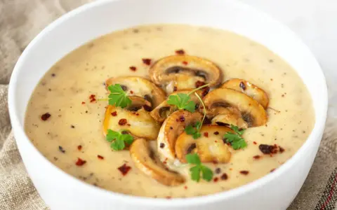 Aksamitny zupa krem z pieczarek, udekorowana plasterkami pieczarek, natką pietruszki i płatkami chili. Idealna na chłodne dni.