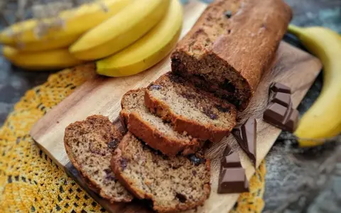 Pyszny chlebek bananowy z czekoladą, pokrojony na kromki, obok świeże banany i kawałki czekolady.
