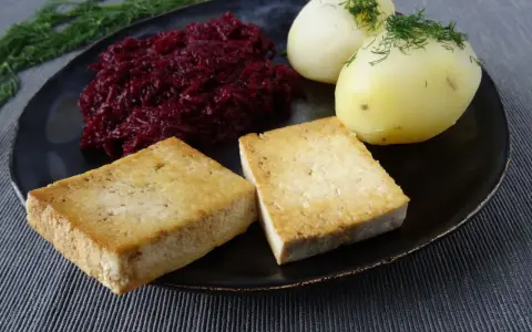 Złociste kotlety z tofu, ziemniaki z koperkiem i buraczki na talerzu.