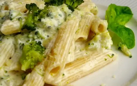 Penne z brokułami w kremowym sosie serowym, udekorowane listkiem bazylii. Pyszne danie, które zachwyci każdego smakosza.