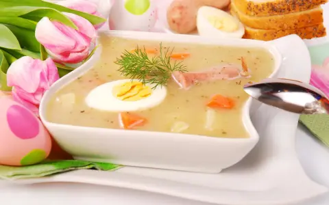 Biały barszcz z jajkiem, kiełbasą, marchewką i koprem, ozdobiony tulipanami i pisankami.