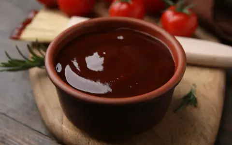 Gęsty, ciemny sos pieczeniowy w glinianej miseczce. Idealny przepis, jak zrobić sos pieczeniowy bez mięsa, z pomidorami i rozmarynem w tle.