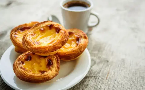 Na talerzyku leżą trzy chrupiące pastéis de nata, obok filiżanka kawy. Idealny poranek.