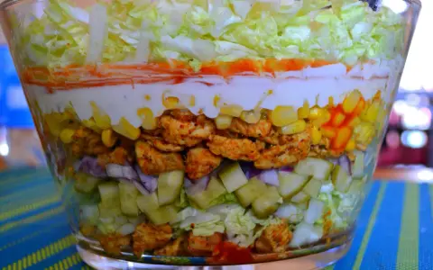 Warstwowa sałatka z kurczakiem w stylu gyros, z kukurydzą, ogórkiem, cebulą i sosem.