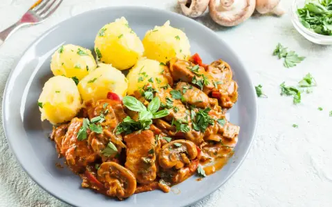 Gulasz drobiowy z pieczarkami i ziemniakami na talerzu, ozdobiony natką pietruszki.