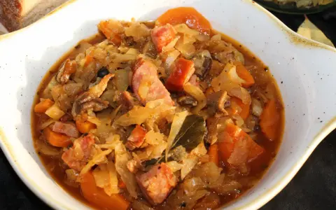 Pyszny bigos ze słodkiej kapusty z kiełbasą i marchewką, podany w białej misie.