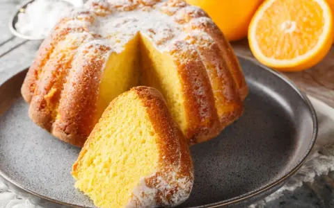 Puszysta babka na oleju, oprószona cukrem pudrem, z pomarańczami w tle. Idealna na niedzielne popołudnie.