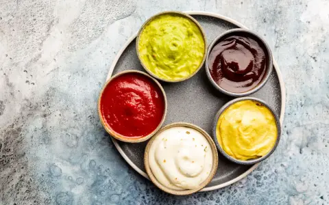 Sześć miseczek z sosami: zielony guacamole, czerwony ketchup, ciemny barbecue, żółta musztarda i biały majonez. Idealne do dań, gdy zastanawiasz się, jak zrobić sos.