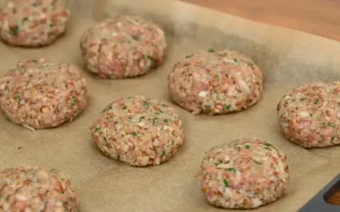 Surowe burgery z piekarnika, przygotowane z mielonego mięsa i kaszy, leżą na papierze do pieczenia.