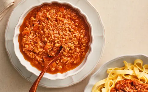 Gęsty, aromatyczny sos do spaghetti bolognese w miseczce, obok porcji makaronu tagliatelle.