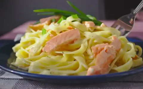 Pyszny makaron z łososiem, udekorowany szczypiorkiem, czeka na widelcu.