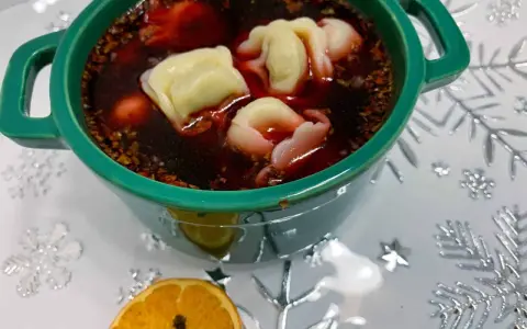 Aromaticzny barszcz z uszkami w zielonej miseczce, ozdobiony suszoną pomarańczą i goździkami.