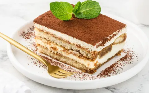 Pyszne tiramisu z mascarpone i śmietaną, posypane kakao i ozdobione miętą. Złoty widelec czeka na pierwszy kęs.