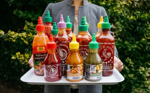 Taca z wieloma butelkami sosu Sriracha o różnych kolorach nakrętek.