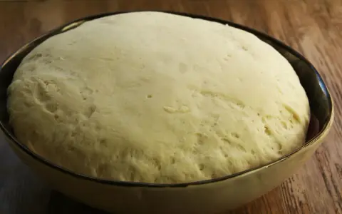 Puszyste ciasto na pizzę wyrosło w misce, gotowe do dalszej obróbki.