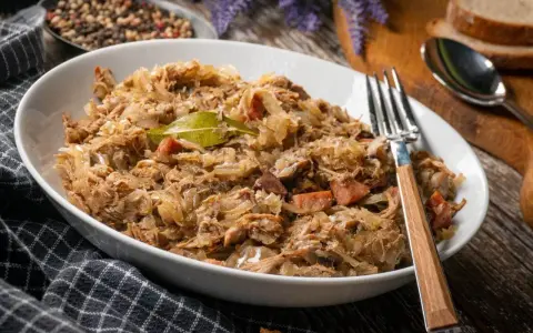 Pyszny bigos w białej misce, z widelcem. Zastanawiasz się, ile może stać bigos w lodówce? Nawet kilka dni, a smakuje coraz lepiej!