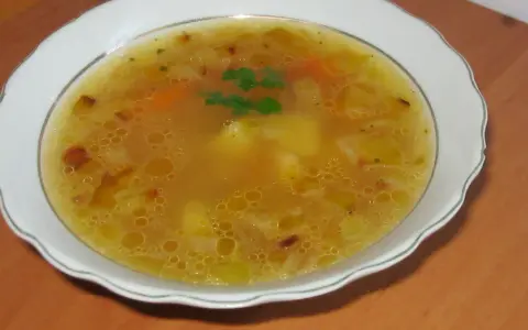Prosta zupa cebulowa z ziemniakami, z kawałkami marchewki i natką pietruszki, podana w białej misce.