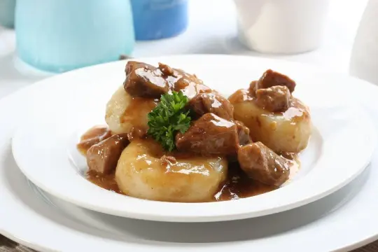 Kluski śląskie z gęstym, aromatycznym sosem mięsnym i gałązką natki pietruszki. Pyszny sos do kluski śląskie.
