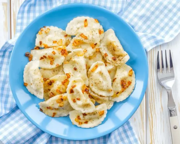 Pyszne pierogi z soczewicą czerwoną, posypane skwarkami i pieprzem, na niebieskim talerzu.