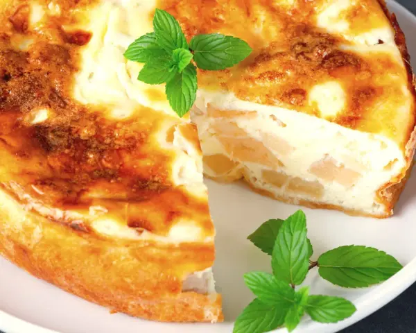 Pyszne ciasto z serka wiejskiego z kawałkami owoców, udekorowane listkami mięty.