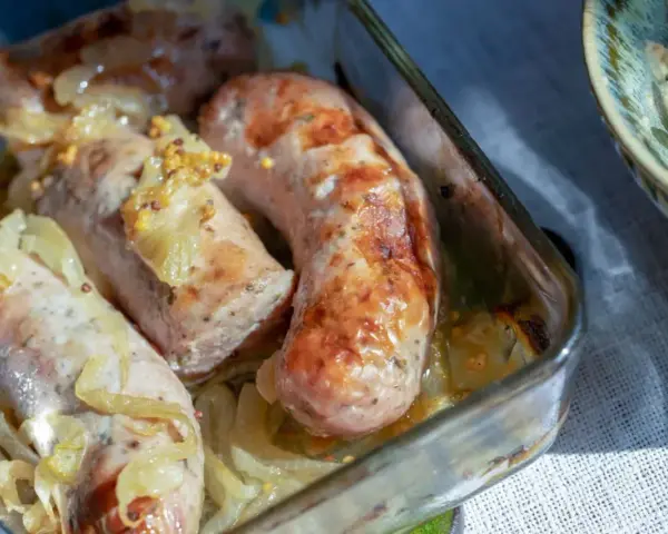 Biała kiełbasa pieczona z cebulką i musztardą w szklanym naczyniu. Apetyczny zapach unosi się w powietrzu.