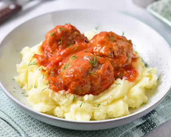 Pyszne pulpeciki w sosie pomidorowym na kremowym purée ziemniaczanym, posypane świeżym koperkiem.
