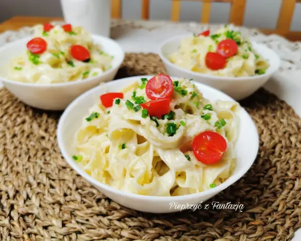 Pyszny makaron tagliatelle w kremowym sosie 4 sery, udekorowany pomidorkami koktajlowymi i szczypiorkiem. Idealny na szybki obiad.
