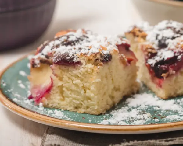 Szybkie ciasto drożdżowe z owocami, posypane cukrem pudrem, na talerzu.