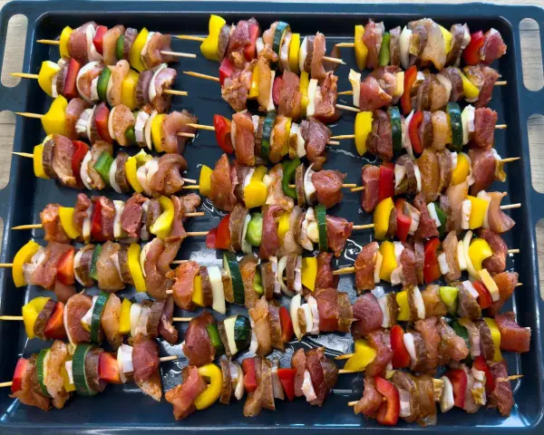Szaszłyki w piekarniku gotowe do pieczenia: mięso, papryka, cebula i cukinia na patyczkach.
