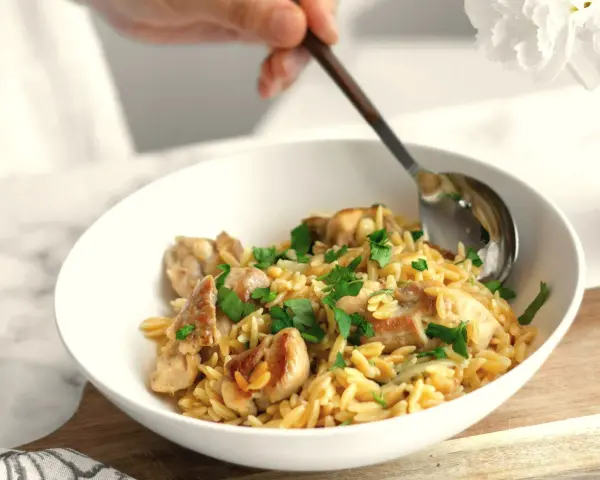 Miseczka pełna makaronu orzo z kawałkami kurczaka i posiekaną natką pietruszki. Idealny szybki sos do makaronu na obiad.